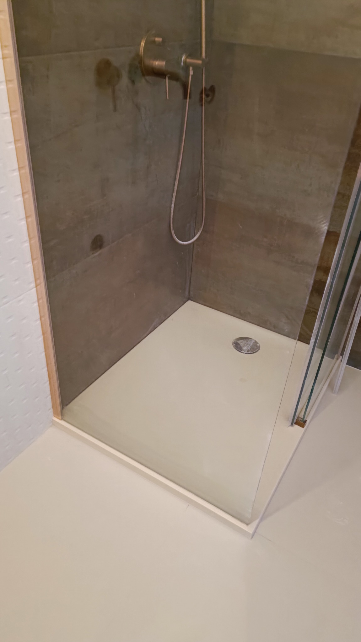 Nowoczesny brodzik z kabiną prysznicową i armaturą w odcieniach brązu, widok z góry na odpływ.