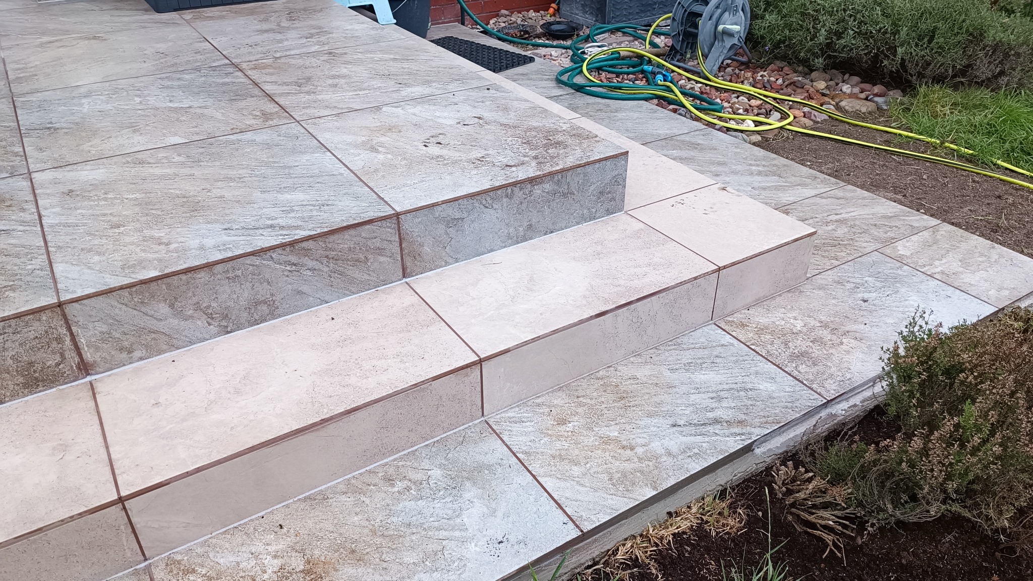 Wykończone płytkami schody zewnętrzne prowadzące do ogrodu, z widoczną fugą i elementami zieleni w tle.