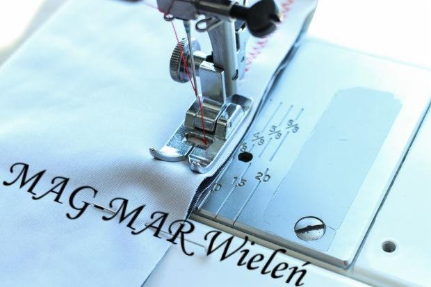 Stopka maszyny do szycia zszywająca biały materiał z nadrukowanym czarnym napisem 'MAG-MAR Wieleń', widoczne czerwone nici.