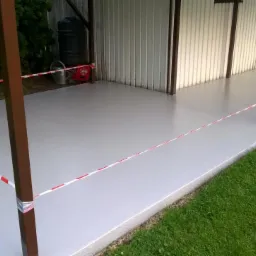 Świeżo wylana, szara posadzka na zewnątrz budynku, zabezpieczona taśmą ostrzegawczą.