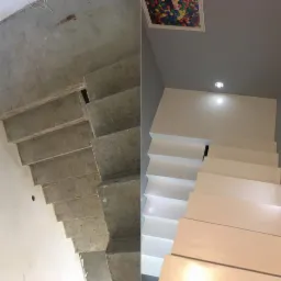 Por&oacute;wnanie stanu surowego betonowych schod&oacute;w z efektem końcowym - białe, minimalistyczne schody w nowoczesnym wnętrzu z oświetleniem punktowym i obrazem na suficie.