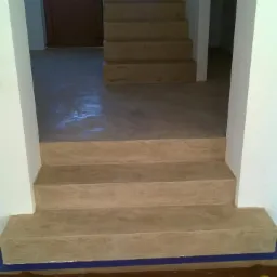 Wykończenie schodów i podłogi z efektem betonu architektonicznego, widoczne niezabezpieczone kable elektryczne i taśma malarska zabezpieczająca podłogę.