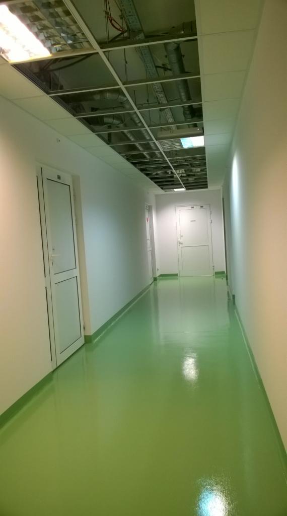 Korytarz z zieloną, błyszczącą posadzką żywiczną, widoczna instalacja pod sufitem podwieszanym.