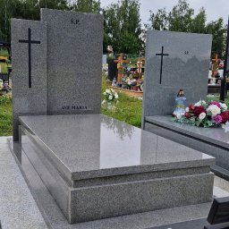 KAMIENIARSTWO ,,KAM-BRUX' nagrobki - Szary, granitowy pomnik z napisem 'Ave Maria' i krzyżem, na cmentarzu, z ławką w prawym dolnym rogu. Widok na nagrobki i drzewa w tle, pochmurne niebo.