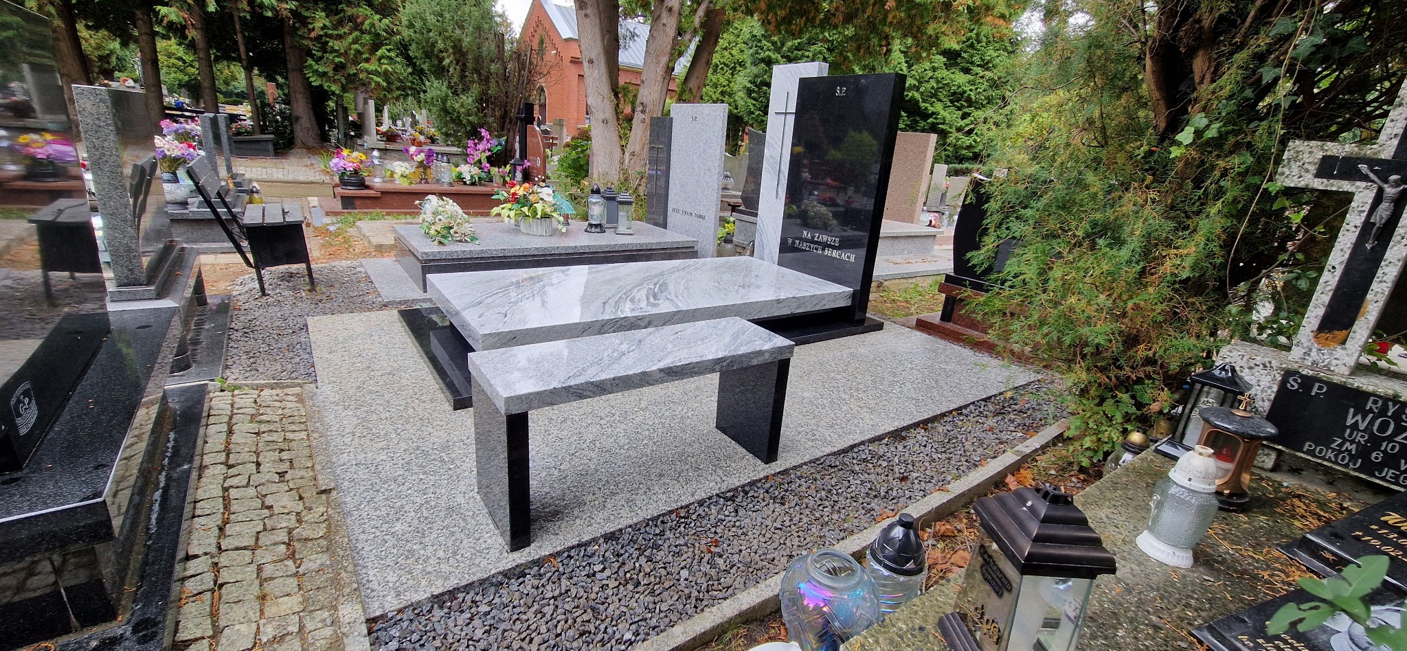 Nowoczesny nagrobek z jasnego granitu z ławką w Świdnicy. Minimalistyczny design, gładkie powierzchnie, otoczenie cmentarza z zielenią i innymi pomnikami.