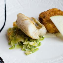 Food Art - Elegancko podane danie: smażona ryba na zielonej sałatce, obok kotlet i plaster jabłka na białym talerzu z dekoracyjnym sosem.