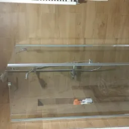 Nowoczesna kabina prysznicowa z drewnopodobnymi płytkami na ścianach, wykończona mozaiką kamienną na krawędzi brodzika, widoczne akcesoria kosmetyczne w niszy ściennej.