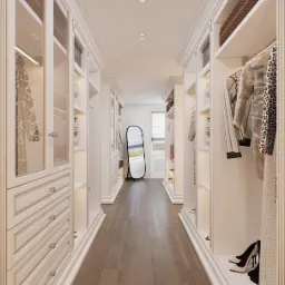Długa garderoba w stylu klasycznym, z białymi szafami z przeszklonymi drzwiami, drewnianą podłogą i wysokim lustrem stojącym na końcu korytarza.