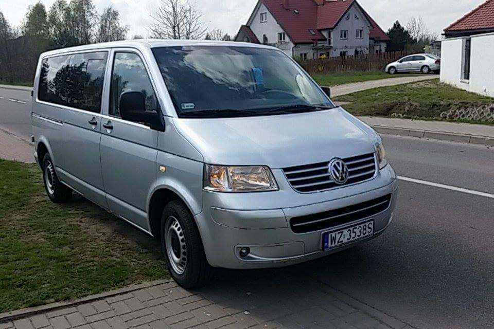 Srebrny Volkswagen Transporter T5 zaparkowany na poboczu, widoczne budynki mieszkalne w tle, tablica rejestracyjna WZ 3538S