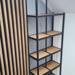 On Yacht - Czarny, metalowy regał z drewnianymi półkami, wykonany w Osielsku, ustawiony na poddaszu, na tle drewnianej ściany z pionowych listew i szarej ściany ze skosem.