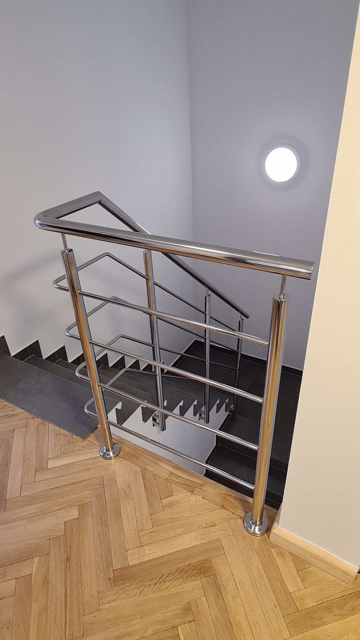 Klatka schodowa z drewnianą podłogą w jodełkę i nowoczesną balustradą ze stali nierdzewnej z poziomymi poprzeczkami, widok z góry.