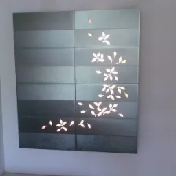 Ściana wyłożona szarymi, poziomymi płytkami z motywem białych liści, tworzącymi delikatny wzór roślinny.