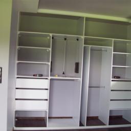 Meble Na Wymiar WNW - Wnętrze białej, otwartej szafy wnękowej z szufladami i drążkami na ubrania, widoczny wkrętak na półce podczas montażu.