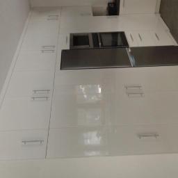 Meble Na Wymiar WNW - Wysoka zabudowa kuchenna z białymi, lakierowanymi frontami, zawierająca wbudowany piekarnik i lodówkę, z subtelnymi, podłużnymi uchwytami.