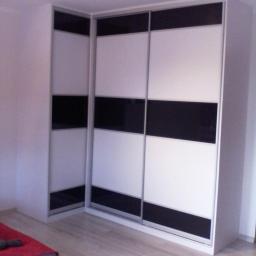 Meble Na Wymiar WNW - Narożna szafa przesuwna z białymi i czarnymi panelami, widoczna na tle drewnianej podłogi w jasnym pomieszczeniu.