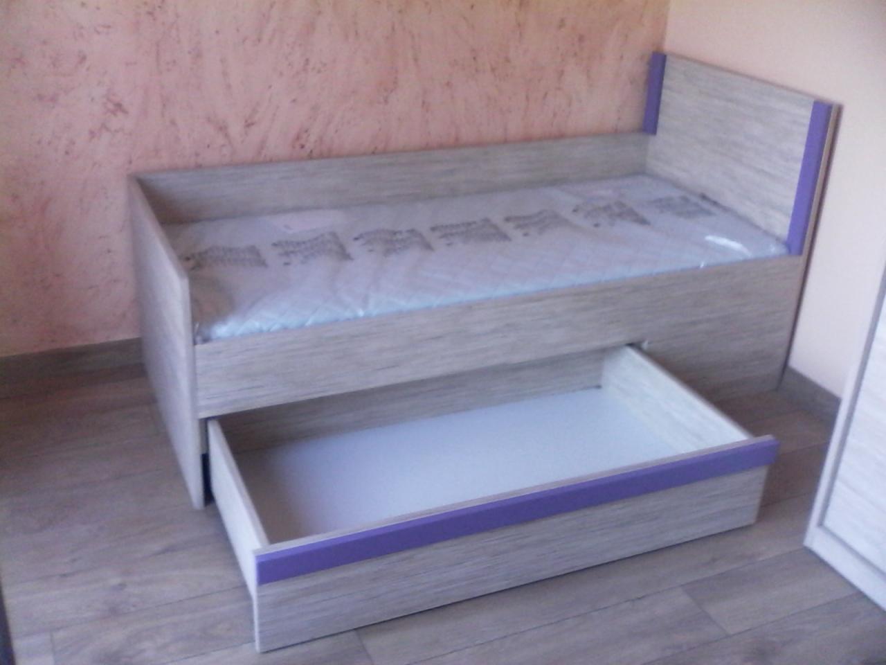 Łóżko dziecięce z szufladą, wykończone drewnopodobną okleiną w odcieniach szarości, z fioletowymi akcentami, materac w folii ochronnej.