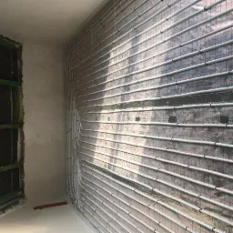 Ułożone rury ogrzewania podłogowego na siatce z folią aluminiową, widok na fragment ściany i okno w surowym stanie.