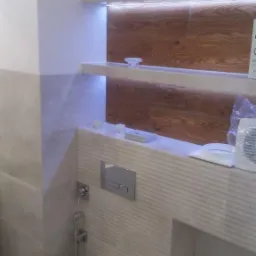 Nowoczesna łazienka z podświetlanymi półkami i drewnianym panelem dekoracyjnym za toaletą podwieszaną, szarymi płytkami na ścianach oraz akcesoriami łazienkowymi.