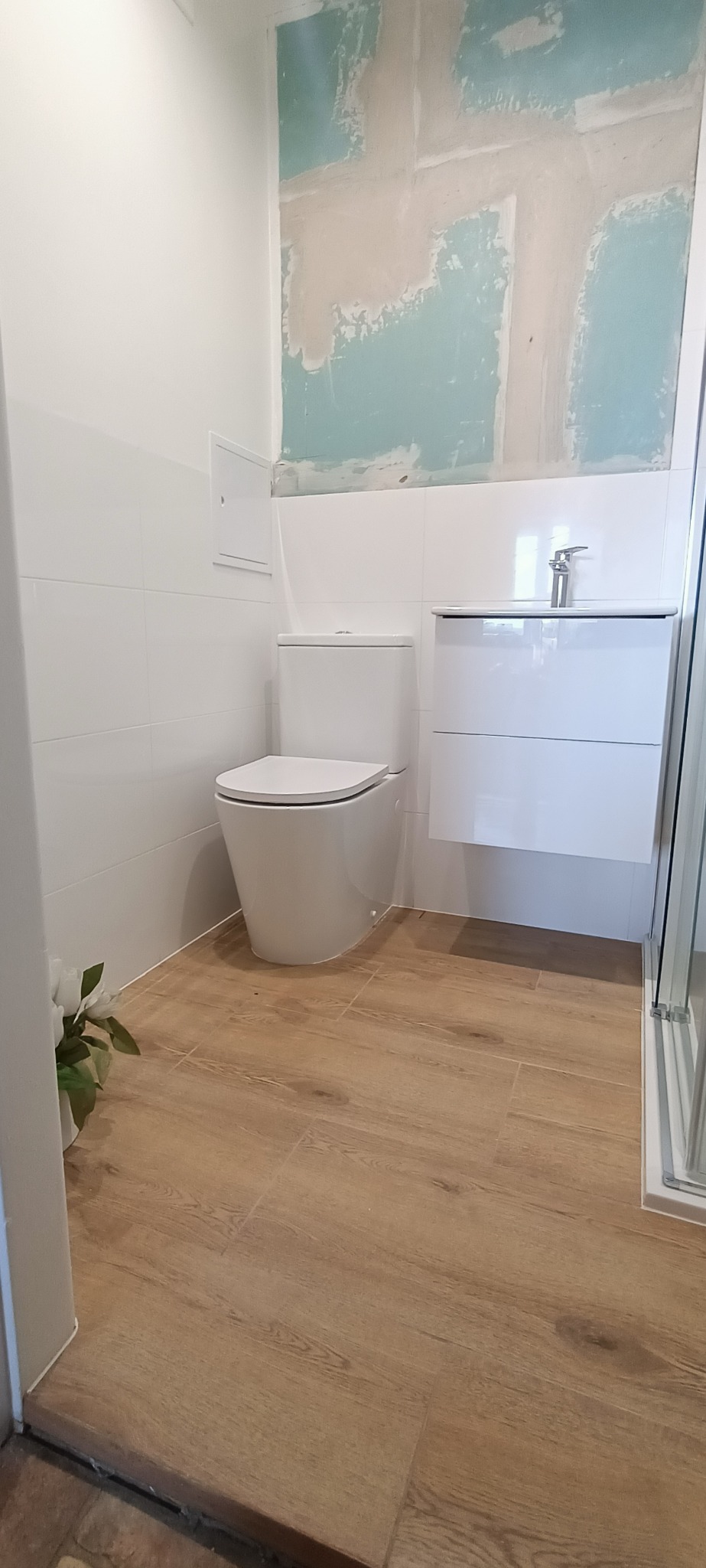 Nowoczesna łazienka w trakcie remontu: biała armatura, drewnopodobne płytki, częściowo wykończone ściany z widocznymi śladami po pracach przygotowawczych.