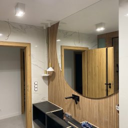 JM STUDIO Jacek Jabłoński, Marcin Pająk - Łazienka w trakcie wykańczania: widoczna zabudowa umywalkowa w czarnym kolorze, lustro w okrągłej ramie z drewnianych listewek, marmurowe płytki na ścianie oraz wisząca lampa z białym kloszem.
