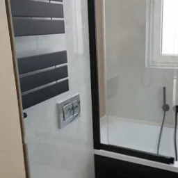 Nowoczesna łazienka z podwieszaną toaletą, grzejnikiem drabinkowym w kolorze antracytowym i kabiną prysznicową z czarnymi profilami.