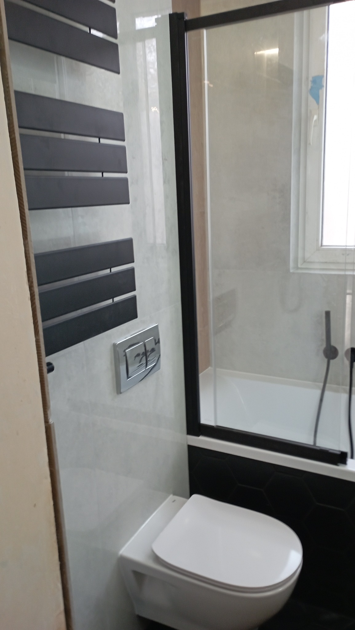 Nowoczesna łazienka z podwieszaną toaletą, grzejnikiem drabinkowym w kolorze antracytowym i kabiną prysznicową z czarnymi profilami.