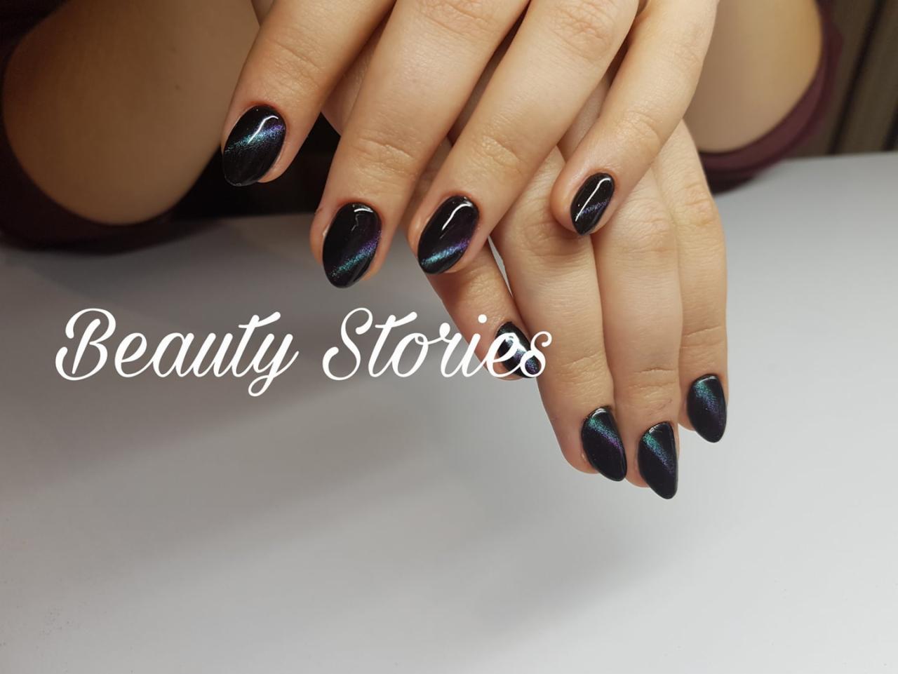 Dłonie z owalnymi paznokciami pomalowanymi ciemnym lakierem z efektem 'kociego oka', widoczny napis 'Beauty Stories'.