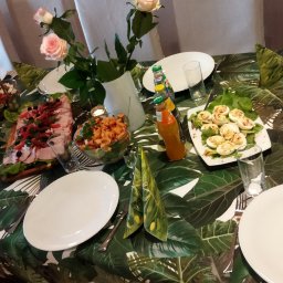 KAERTUR SPÓŁKA Z OGRANICZONĄ ODPOWIEDZIALNOŚCIĄ - Stół z przekąskami na przyjęciu: sałatki, jajka faszerowane, deska serów, napoje. Dekoracja stołu z motywem liści. Kompozycja kwiatowa z różowych róż.