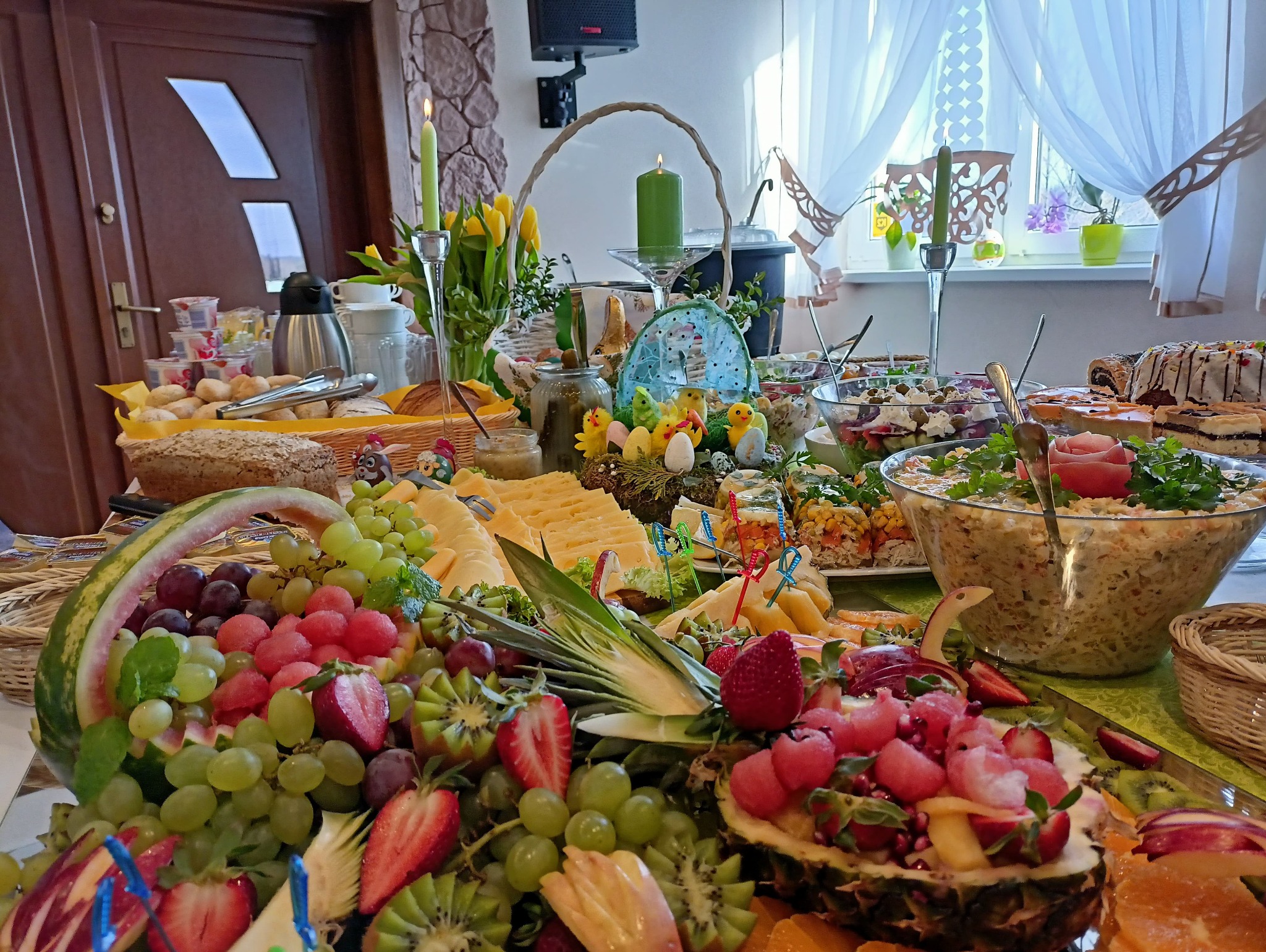 Świąteczny stół w Bolesławowie uginający się pod ciężarem potraw: sałatki, ciasta, owoce (winogrona, truskawki, kiwi), dekoracje wielkanocne, świece. Bogaty wybór dań.