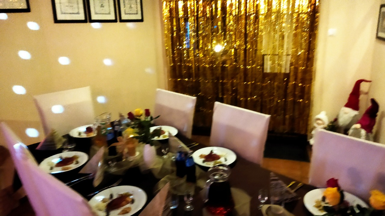 Uroczysty stół z dekoracjami świątecznymi, nakryty dla gości, z elementami dekoracyjnymi w postaci figurek skrzatów i złotych frędzli w tle.