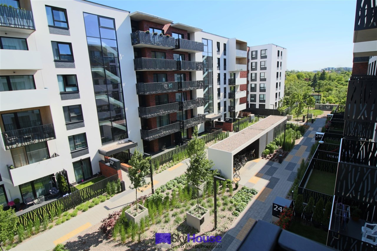 Nowoczesny kompleks apartamentów z balkonami i zagospodarowanym terenem zielonym, widok z góry na ścieżkę rowerową i stojaki na rowery.