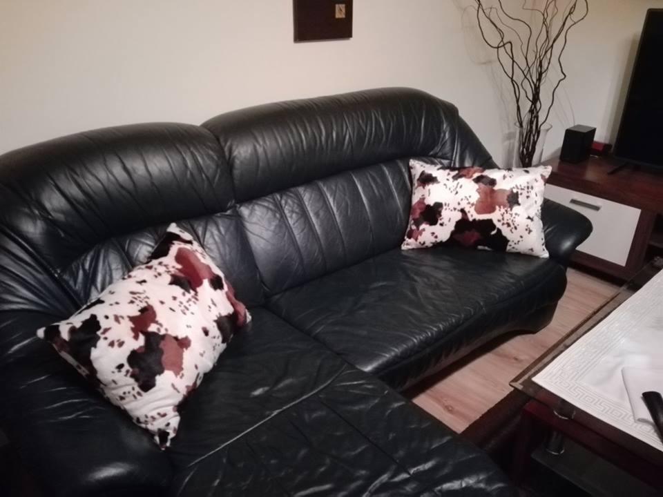 Czarna, skórzana sofa narożna z dwiema poduszkami o wzorze krowich łat, ustawiona w salonie z drewnianą podłogą i minimalistycznym wystrojem.