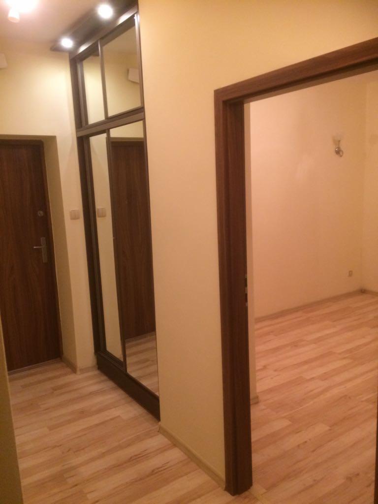 Korytarz po remoncie z drewnopodobną podłogą, widoczne dwie drewniane drzwi i szafa z lustrami.