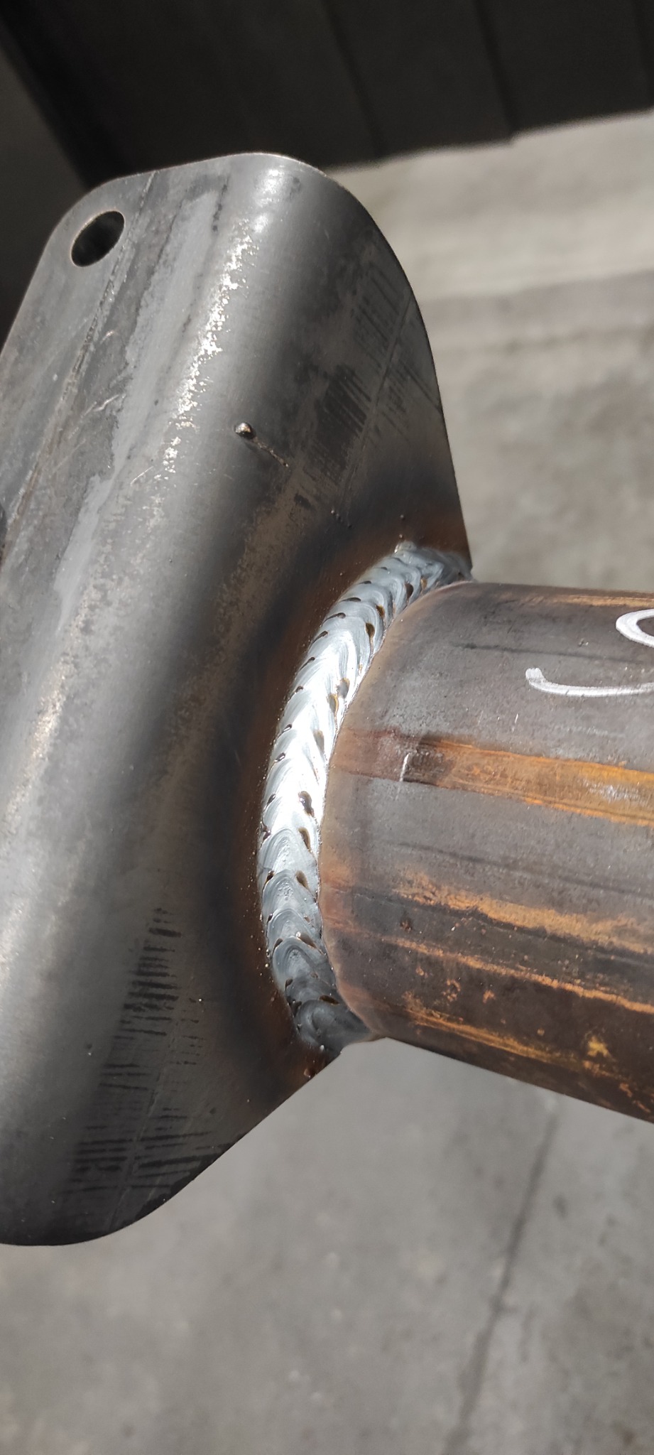 Metalowy element konstrukcyjny połączony spawem; widoczna spoina o regularnej strukturze na styku rury i płaskownika z otworem.