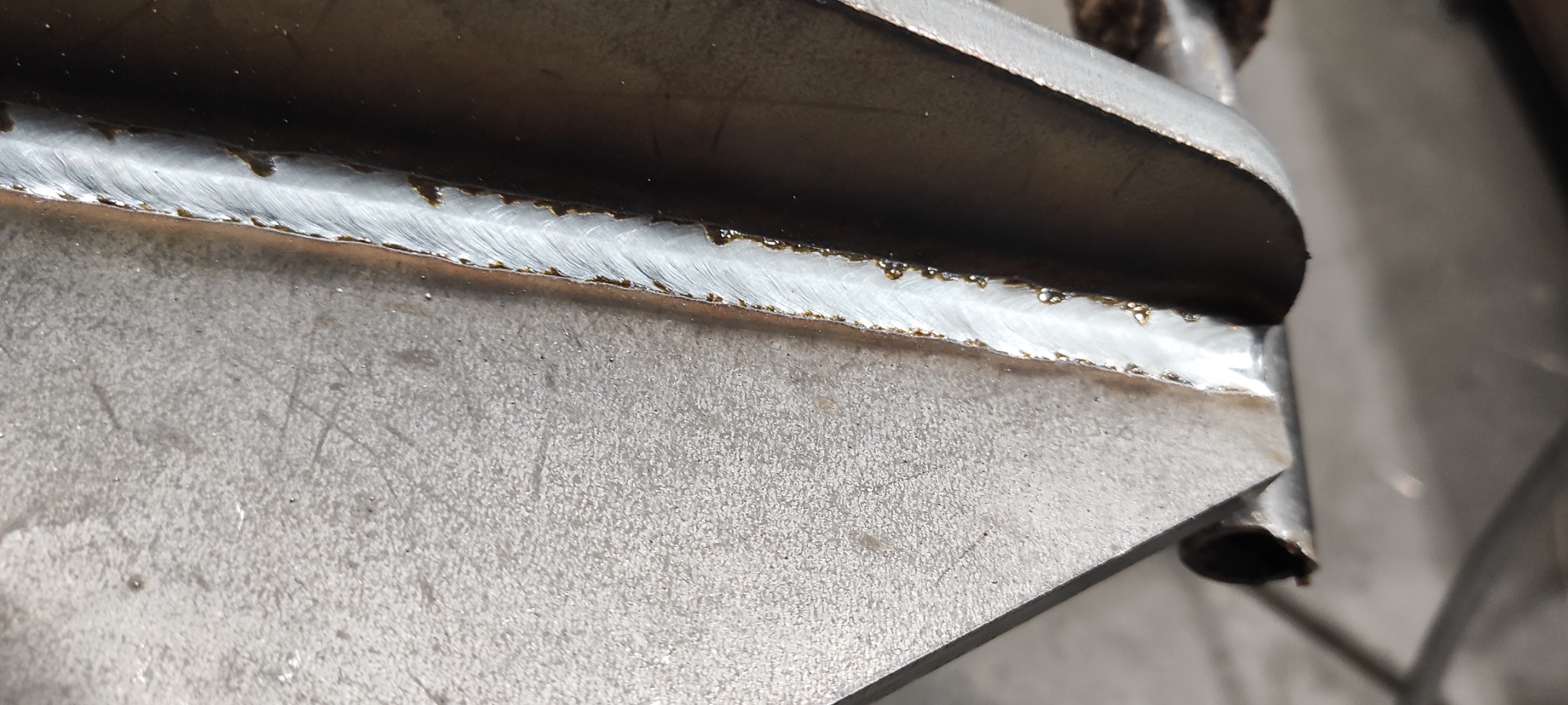 Szczegółowe ujęcie spoiny łączącej dwie metalowe płyty pod kątem, widoczne ślady topnika i nierówności spoiny.