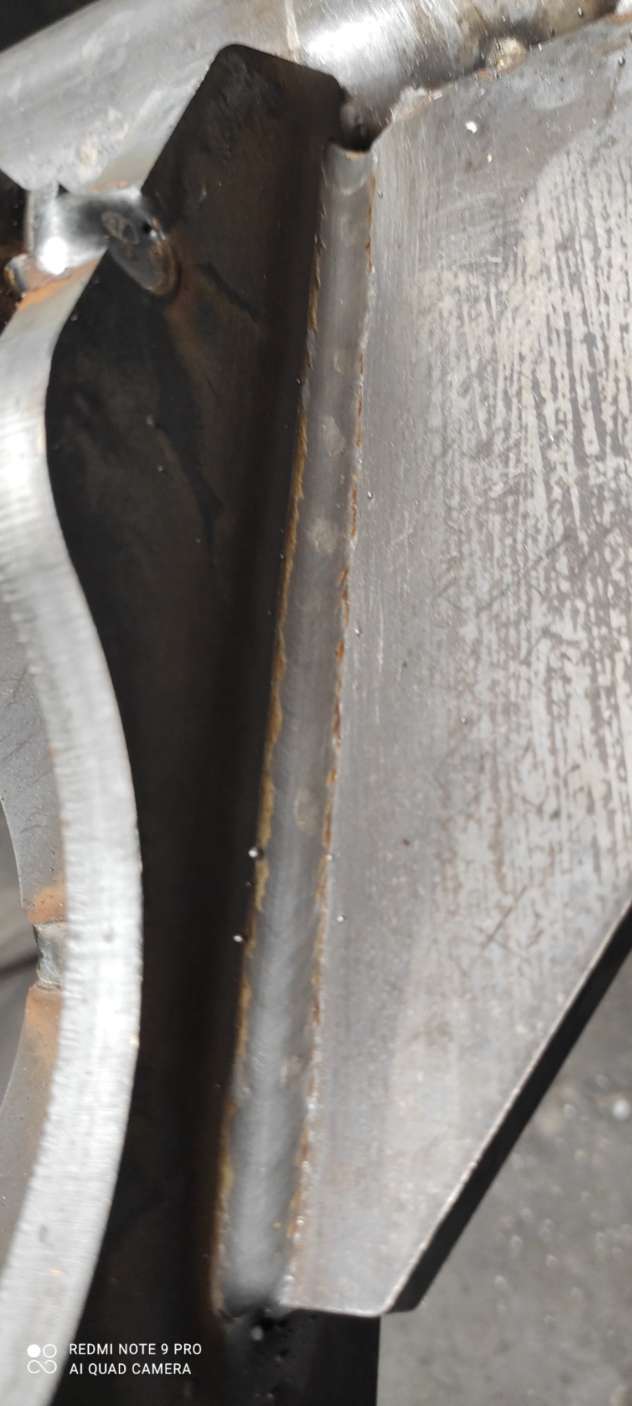 Zbliżenie na fragment konstrukcji metalowej z widocznymi śladami spawania i lekką korozją wzdłuż krawędzi.