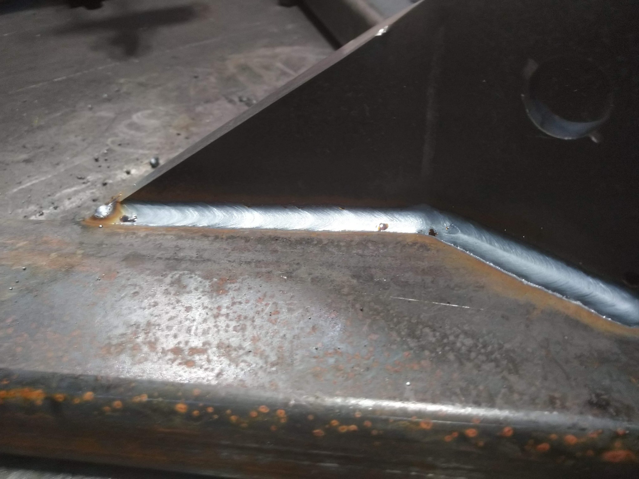 Połączenie spawane dwóch elementów stalowych, widoczny świeży spaw na brudnej, zardzewiałej powierzchni metalu.