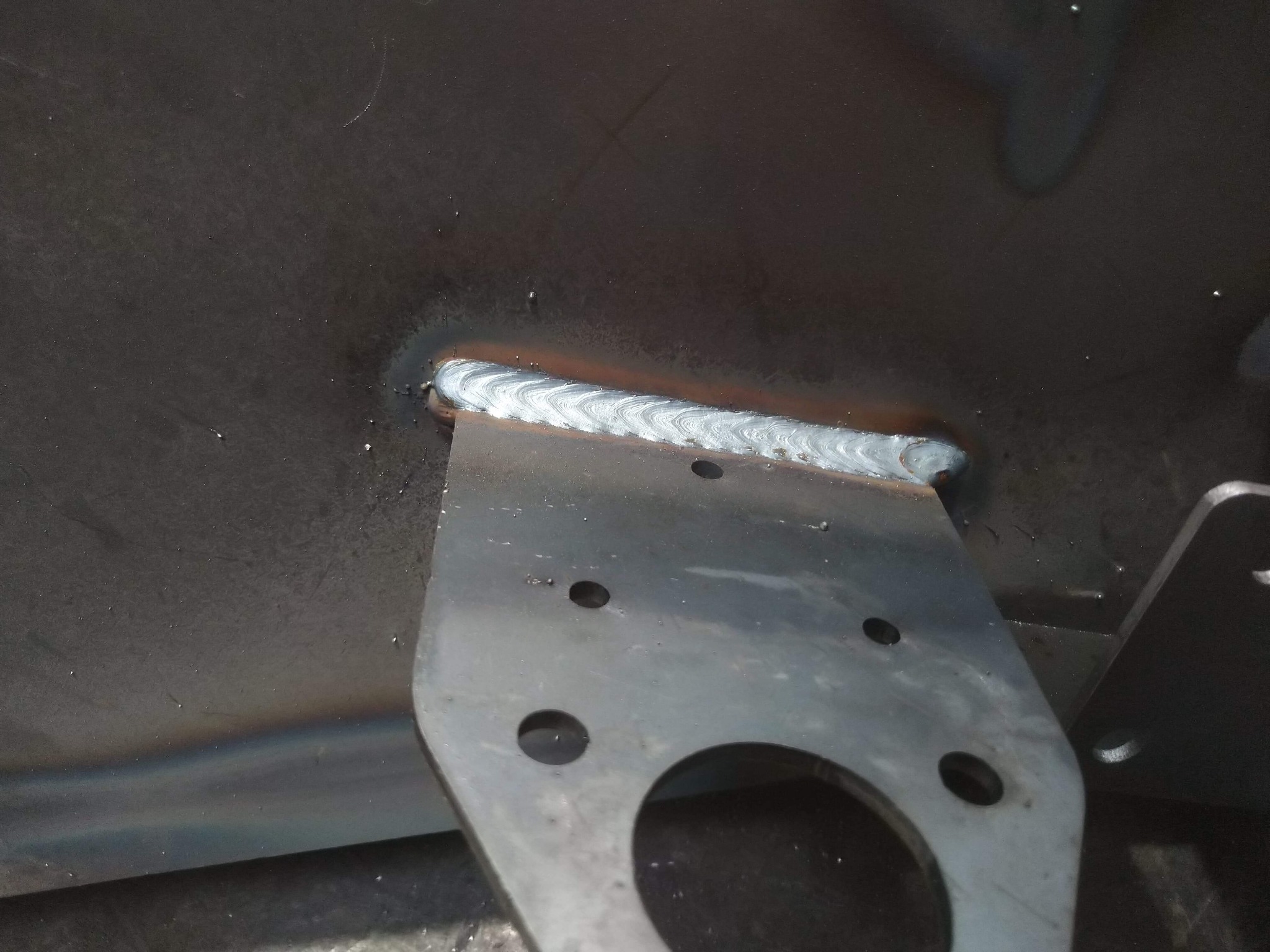 Detal spoiny łączącej metalowy element z blachą, widoczne drobne otwory w elemencie mocującym.