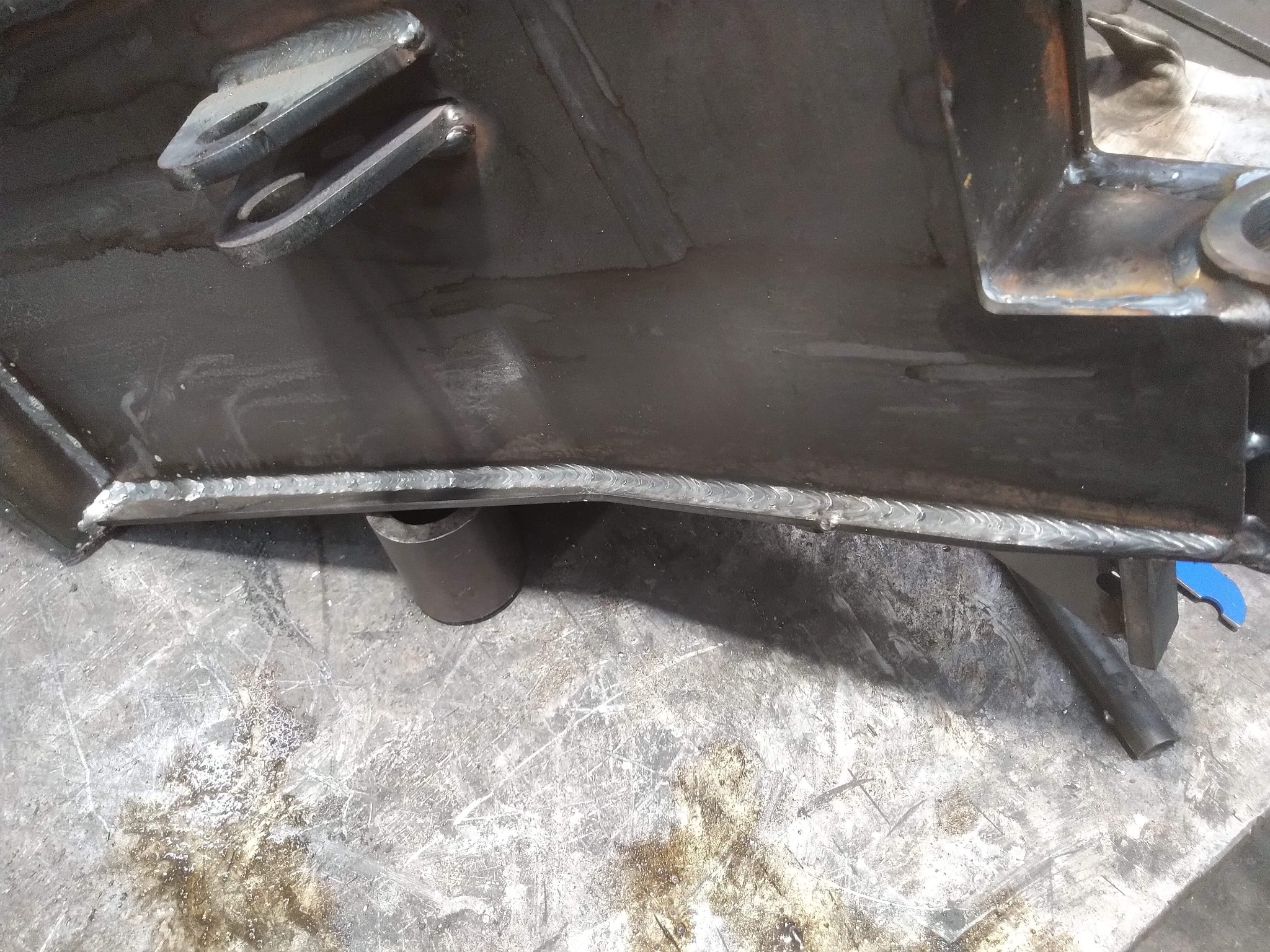 Metalowa konstrukcja z widocznymi spawami, uchwytami i śladami obróbki na brudnym stole warsztatowym.