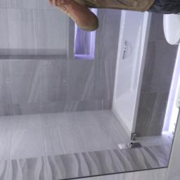 Rem-Bud Bartosz Żemła - Wykończona łazienka z szarymi płytkami imitującymi kamień, z wnęką podświetloną fioletowym światłem, białą wanną i szklanym parawanem nawannowym.