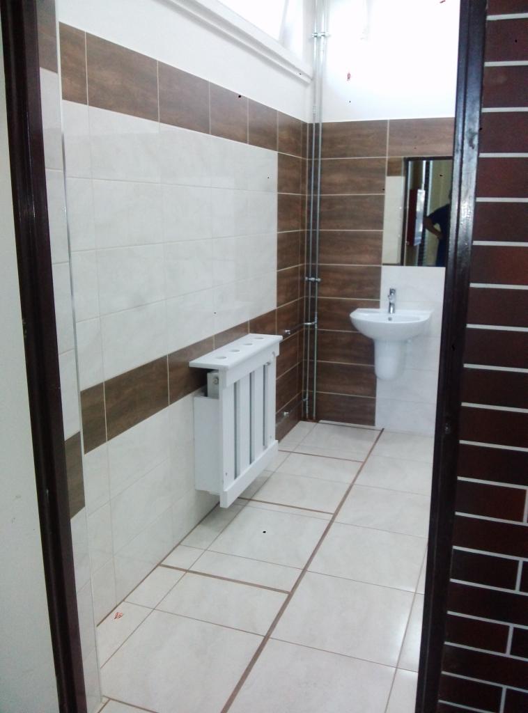 Wyremontowana łazienka z białymi i brązowymi płytkami, białą umywalką na postumencie i grzejnikiem dekoracyjnym z białymi szczebelkami.