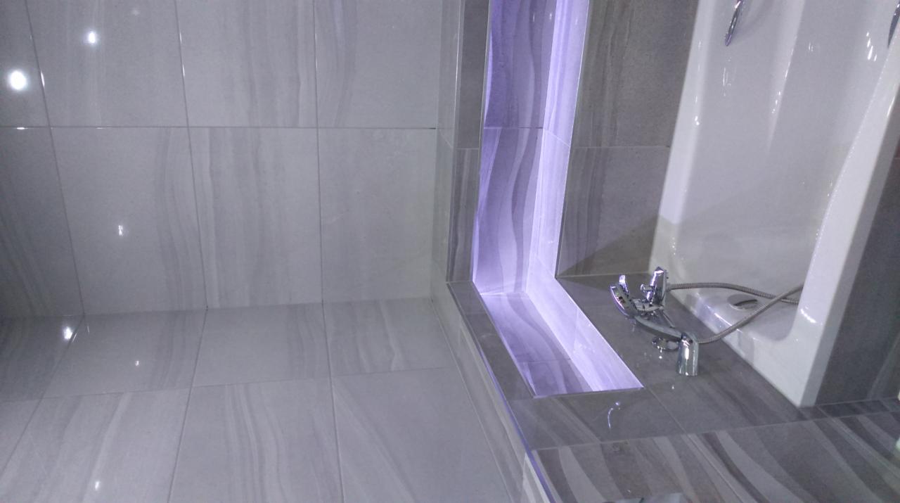 Wykończona łazienka z szarymi płytkami imitującymi marmur, podświetlaną wnęką i nowoczesną armaturą.