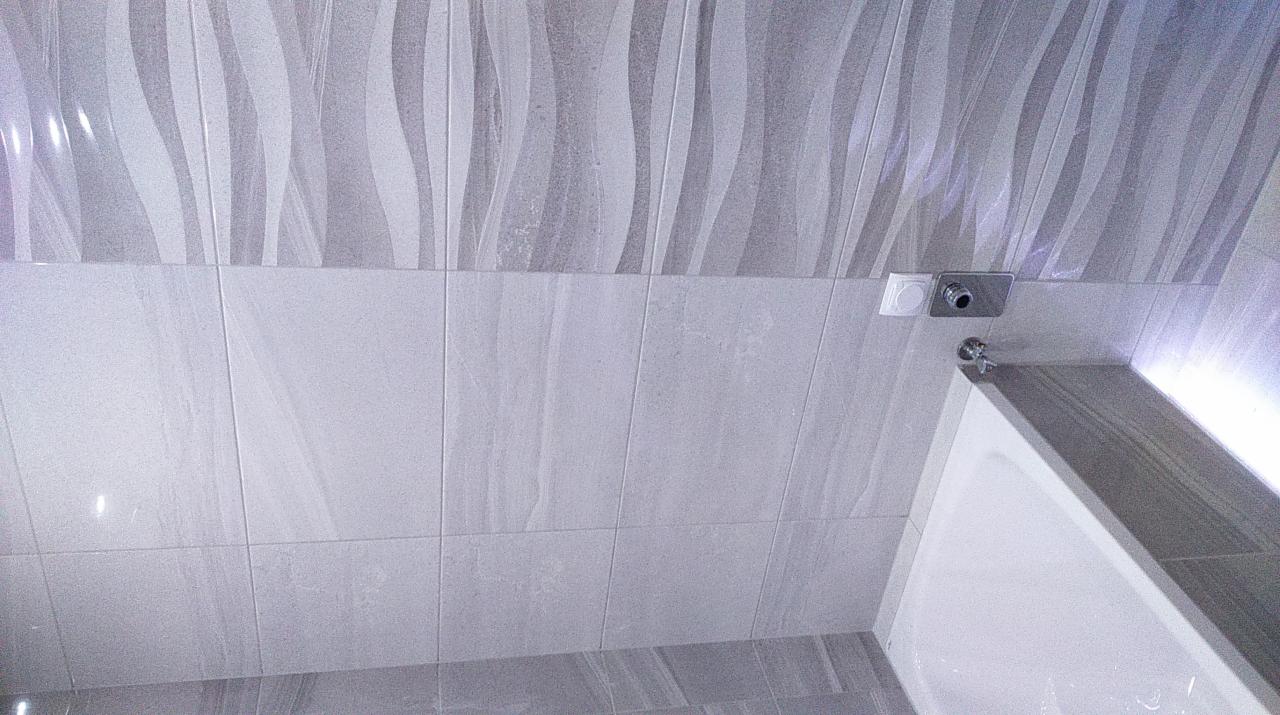 Wykończona łazienka w Ćwiklicach z szarymi płytkami imitującymi fale, widoczny fragment wanny i bateria prysznicowa.