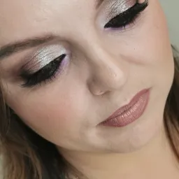 Zbliżenie na twarz kobiety z srebrzystym, brokatowym cieniem na powiekach, mocno wytuszowanymi rzęsami i ustami w odcieniu nude.