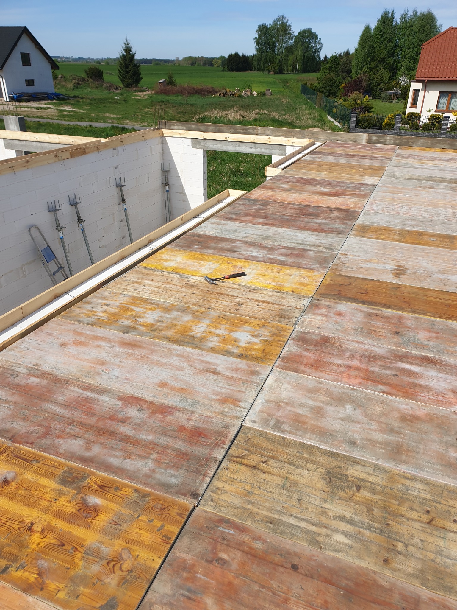 Deskowanie stropu domu w trakcie budowy, widoczne stemple budowlane, białe bloczki oraz młotek.