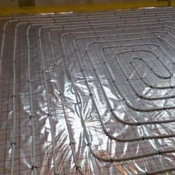 W trakcie montażu ogrzewania podłogowego w Ostrowcu Świętokrzyskim: rury grzewcze ułożone na folii z siatką, widoczne fragmenty ścian i izolacji.