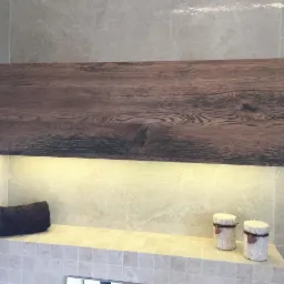 Drewniana półka w łazience z oświetleniem LED, brązowy ręcznik i dwie dekoracyjne świece na kamiennym blacie.