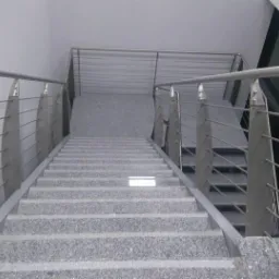 Schody z szarego kamienia z metalową balustradą o nowoczesnym designie, widok z dołu na górę, z oświetleniem wbudowanym w stopień.