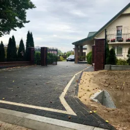 Ułożona kostka brukowa na podjeździe do domu jednorodzinnego z widoczną studzienką drenażową i rozsypanymi kasztanami.