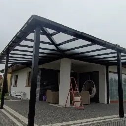 Zadaszenie tarasu z czarną konstrukcją metalową i przezroczystym dachem, widoczne meble ogrodowe i drabina, Mir&oacute;w Stary.